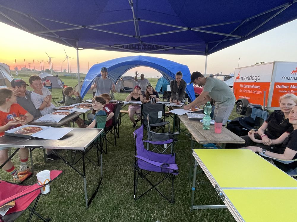 Vereinsmitglieder essen gemeinsam Pizza unter dem Pavillon auf dem Campingplatz Fehmarn