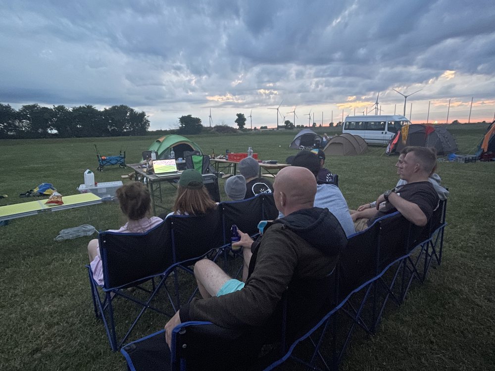 Vereinsmitglieder schauen abends in Campingstühlen gemeinsam Fußball